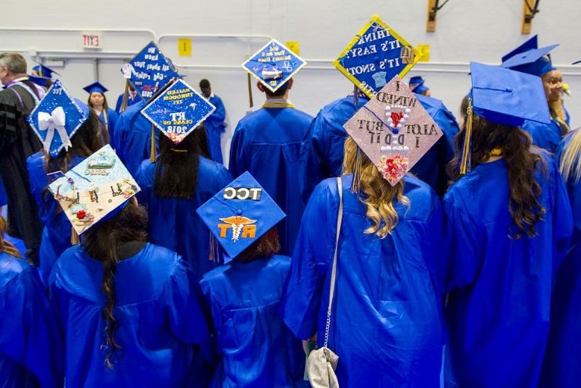 身穿毕业典礼礼服的学生背对着镜头摆姿势, 他们的帽子上写着各种各样的信息